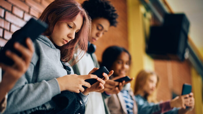 Group of teenagers using mobile phones in hallway at high school.